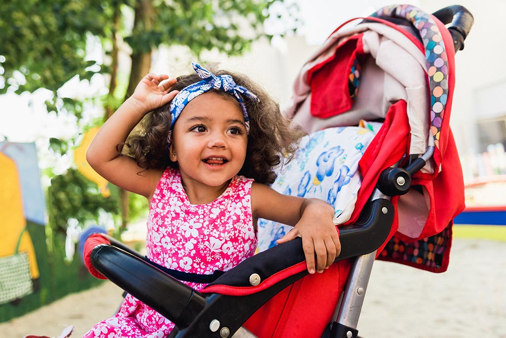 happy little girl with curly hair sitting in a stroller
