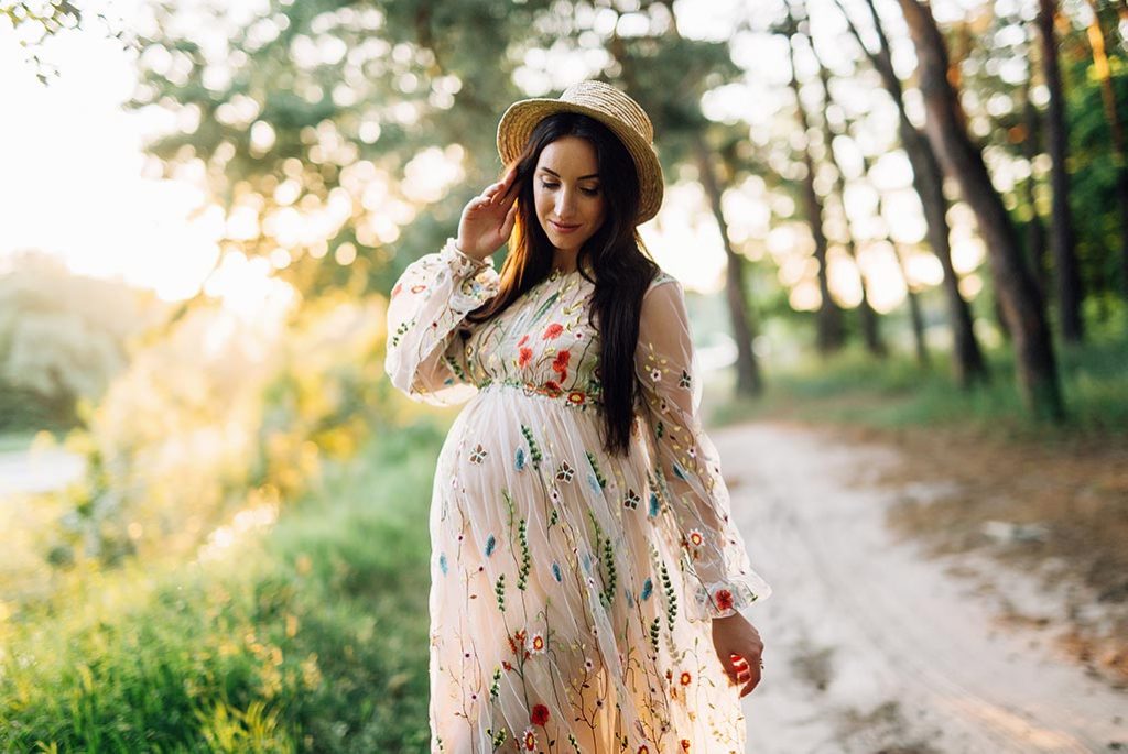 pregnant girl in a long embroidered beige dress and a straw hat